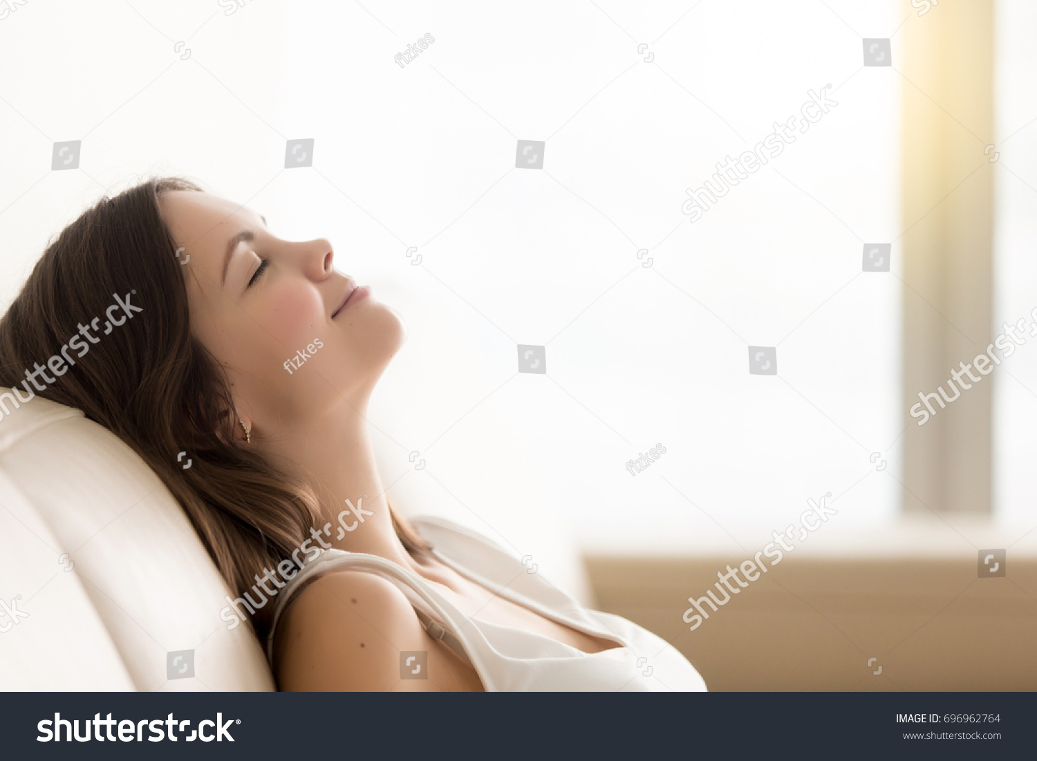 Relaxed young woman enjoying rest on comfortable sofa, calm attractive girl relaxing on couch, breathing fresh air with eyes closed, meditating at home, peace of mind, headshot portrait, copy space #696962764