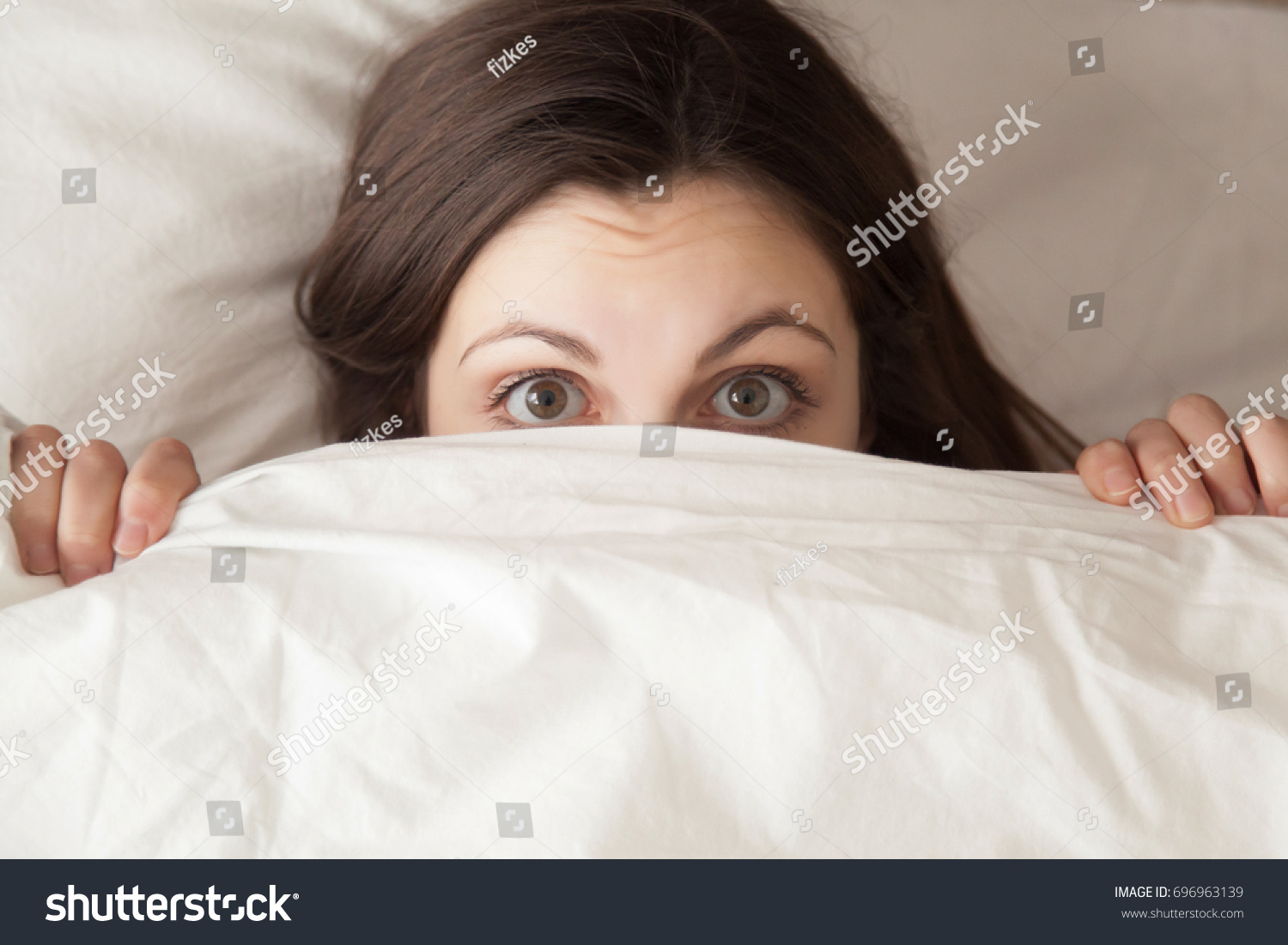 Funny surprised girl covering half of face with white blanket, young scared woman hiding and peeking from duvet, afraid of night monsters, feels embarrassed, wide awake, head shot close up, top view #696963139