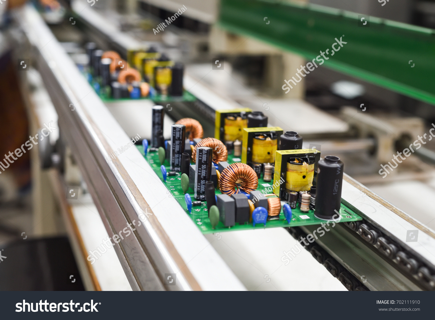 Manual insertion of electronic components on printing circuit board assembly before wave soldering. The image taken in a electronic production plat on a conveyor belt.   #702111910