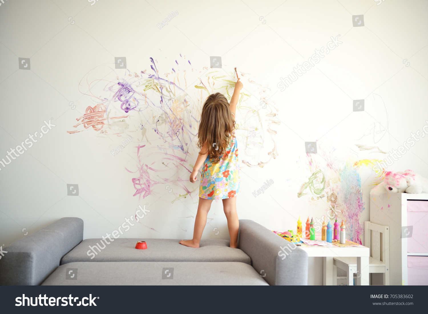 Curly cute little toddler girl painting with paints color and brush on the wall. Works of child #705383602