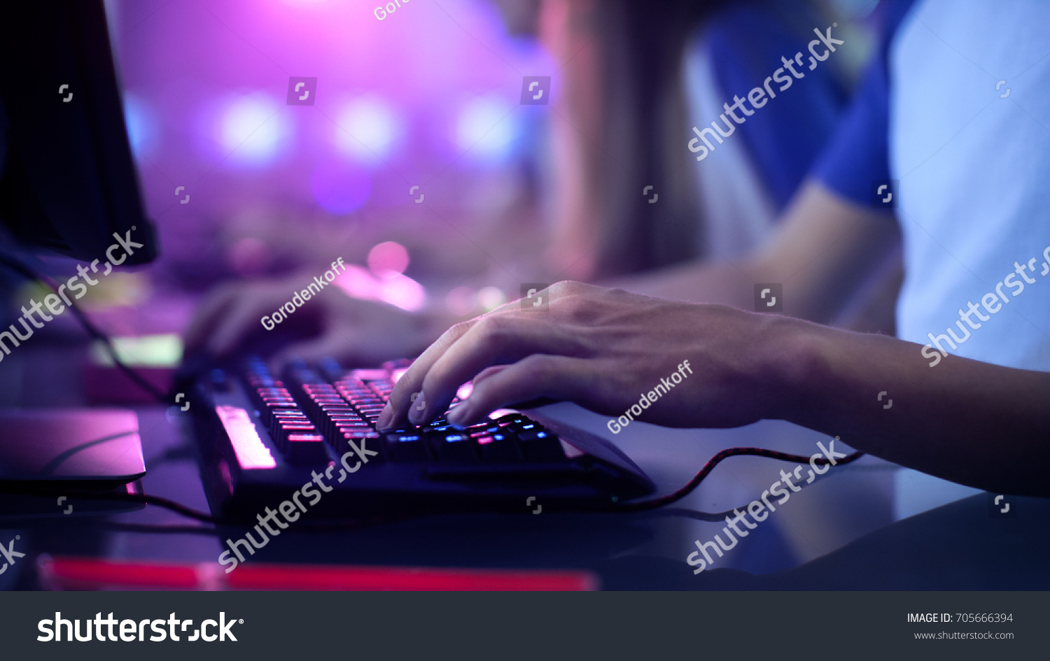 Close-up On Gamer's Hands on a keyboard, Actively Pushing Buttons, Playing MMO Games Online. Background is Lit with Neon Lights. #705666394