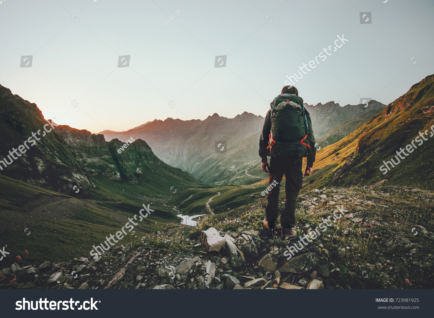 Mann Wandern bei Sonnenuntergang Berge mit schweren Rucksack Reise Lifestyle Wanderlust Abenteuerkonzept Sommerurlaub im Freien allein in die Wildnis #723981925