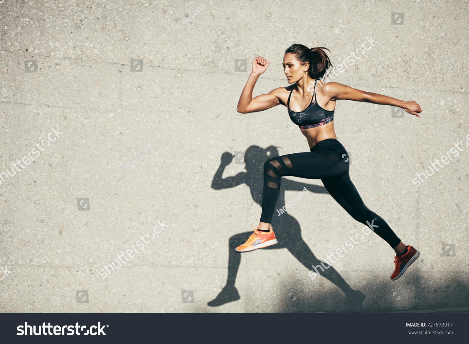 Young woman with fit body jumping and running against grey background. Female model in sportswear exercising outdoors. #727673917