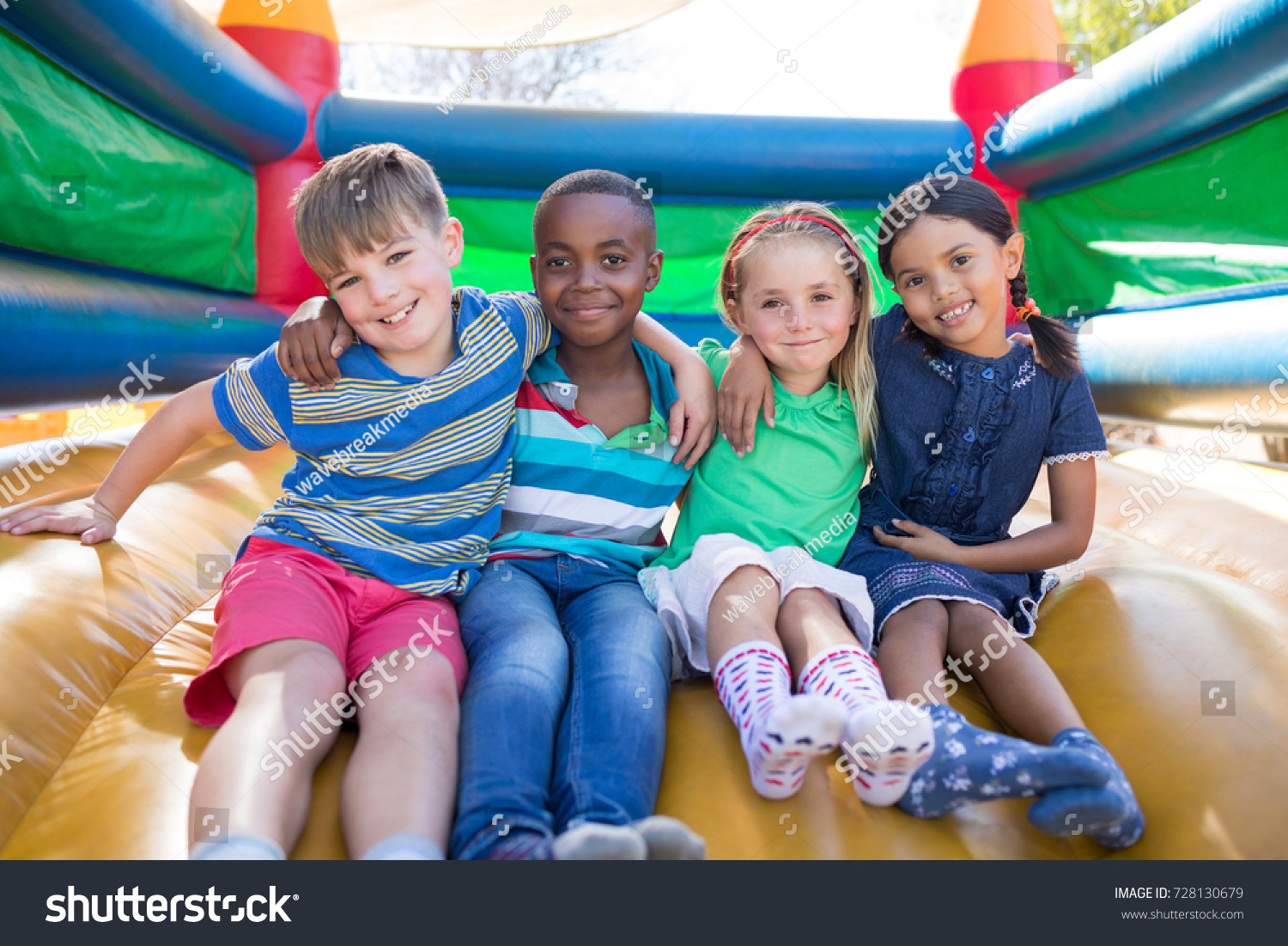 Portrait of friends with arms around sitting on bouncy castle at playground #728130679