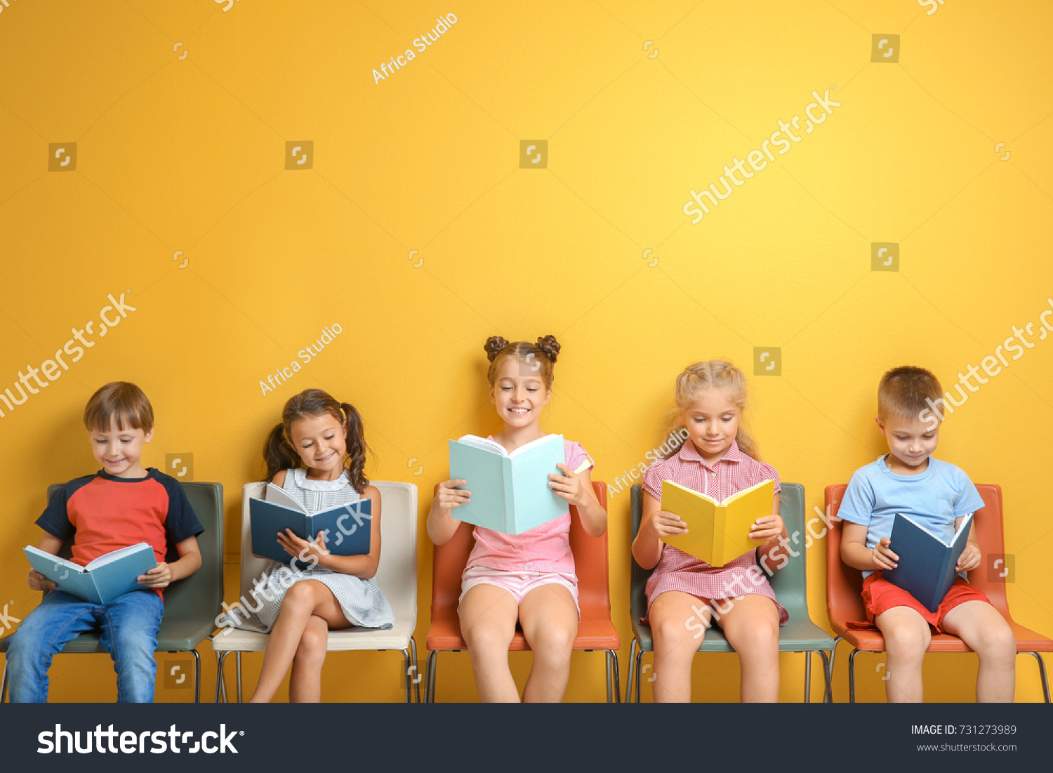 Cute little children reading books while sitting near color wall #731273989