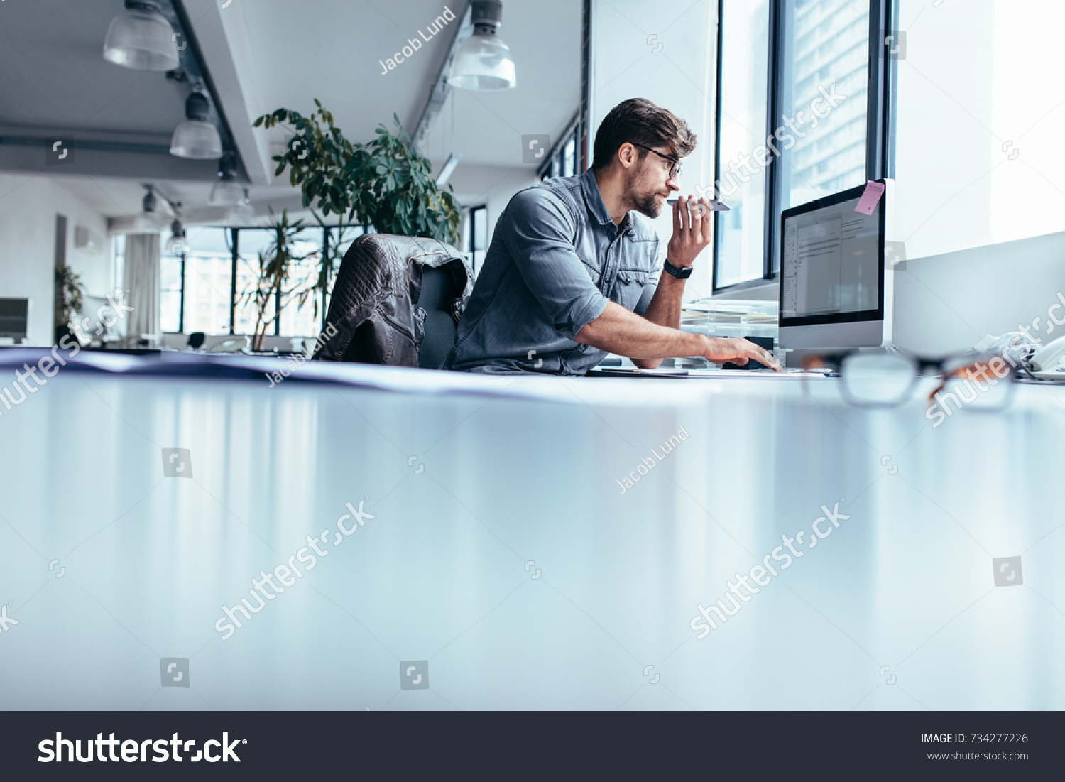 Male executive working on computer and talking on mobile phone. Businessman working in office with phone. #734277226