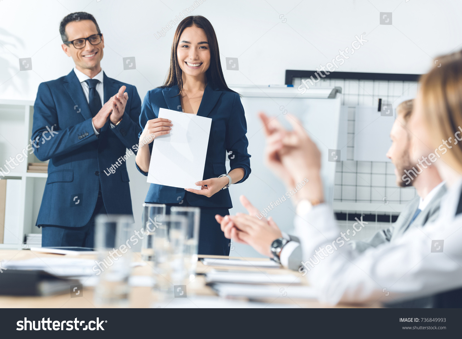 rewarded happy manageress holding blank paper while colleagues clapping to her #736849993