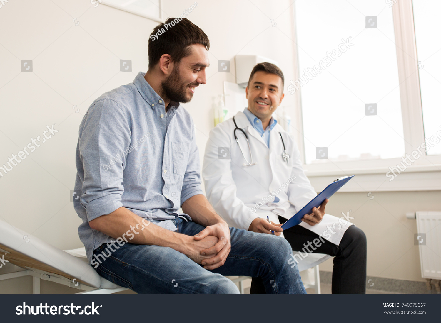 medicine, healthcare and people concept - smiling doctor with clipboard and young man patient meeting at hospital #740979067