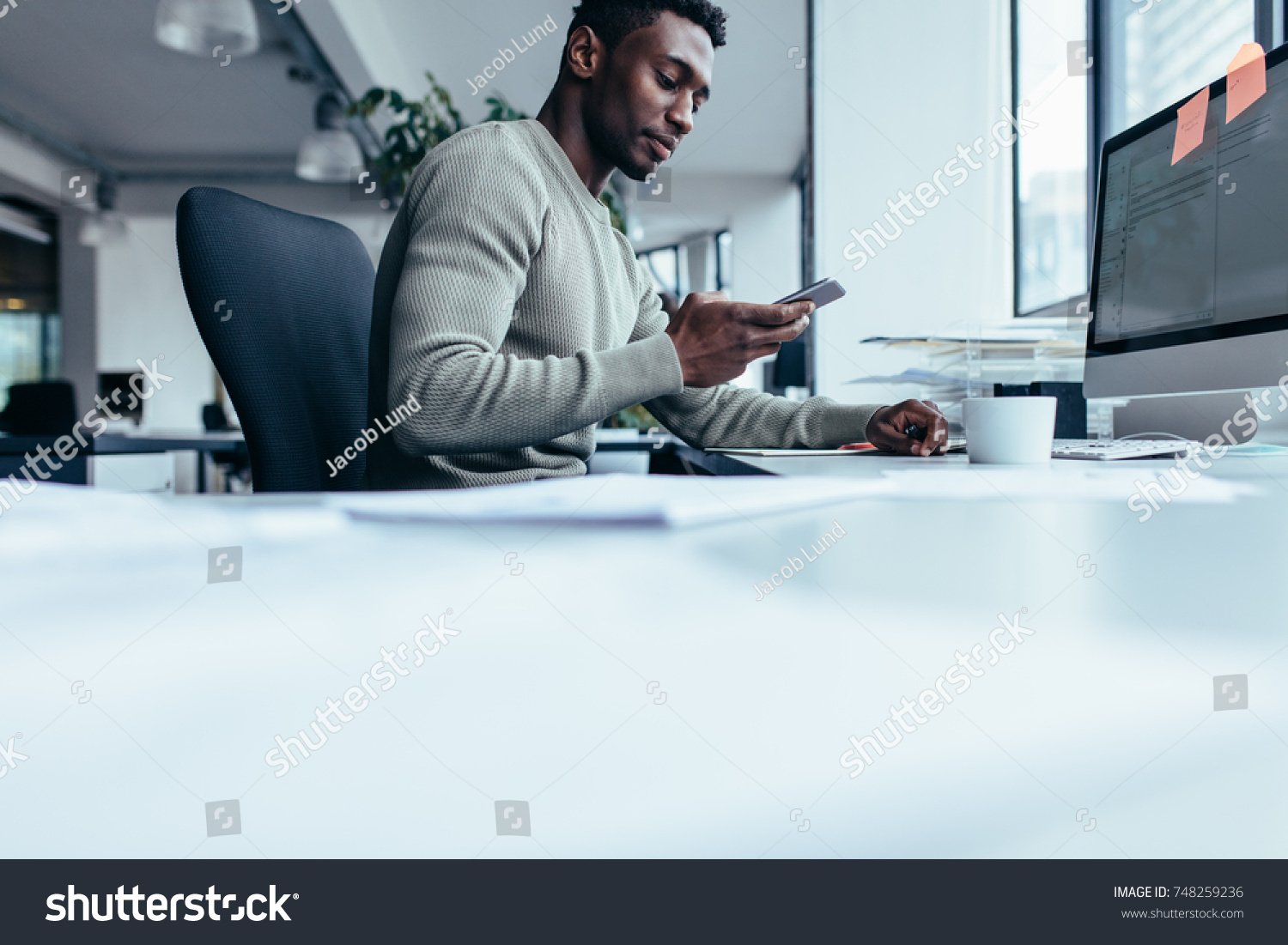 African man using smart phone while sitting at work place. Businessman sitting in modern office. #748259236