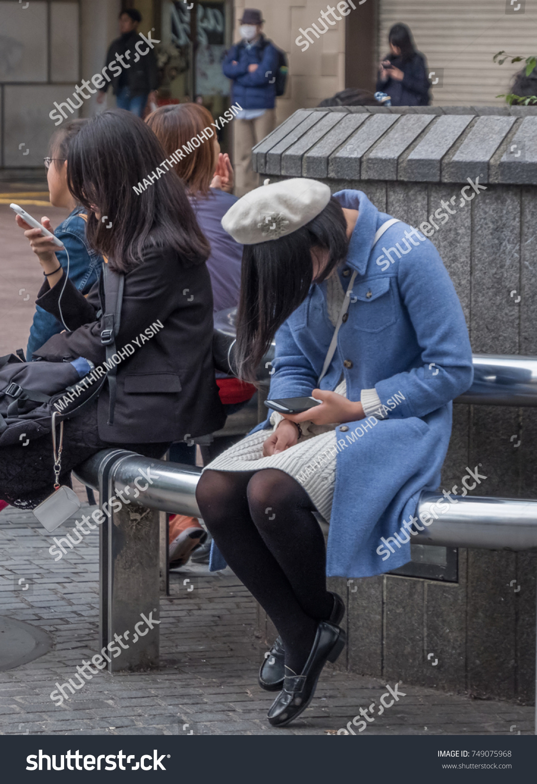 TOKYO, JAPAN - NOVEMBER 4TH, 2017. Young girl with smartphone sitting on a bench in Hachiko square, Shibuya #749075968
