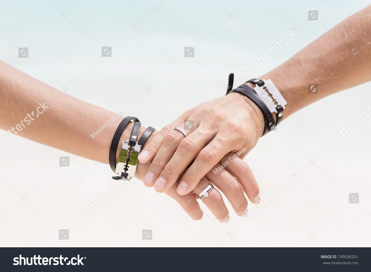 The man's hand hold the woman's hand. Close up hands with beautiful engagement rings. Style wedding. Fashionable couple. Hands with bracelets and blades.  #749536201