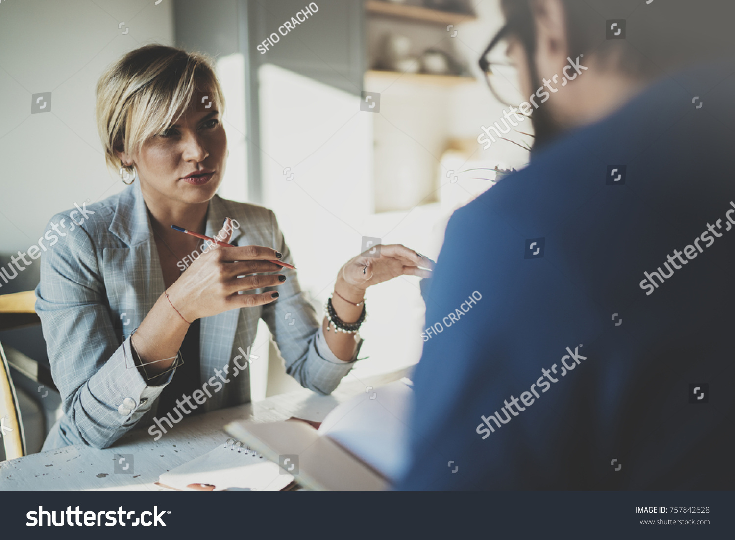 Coworkers working process at home.Young blonde woman working together with bearded colleague man at modern home office.People making conversation together.Blurred background.Horizontal #757842628
