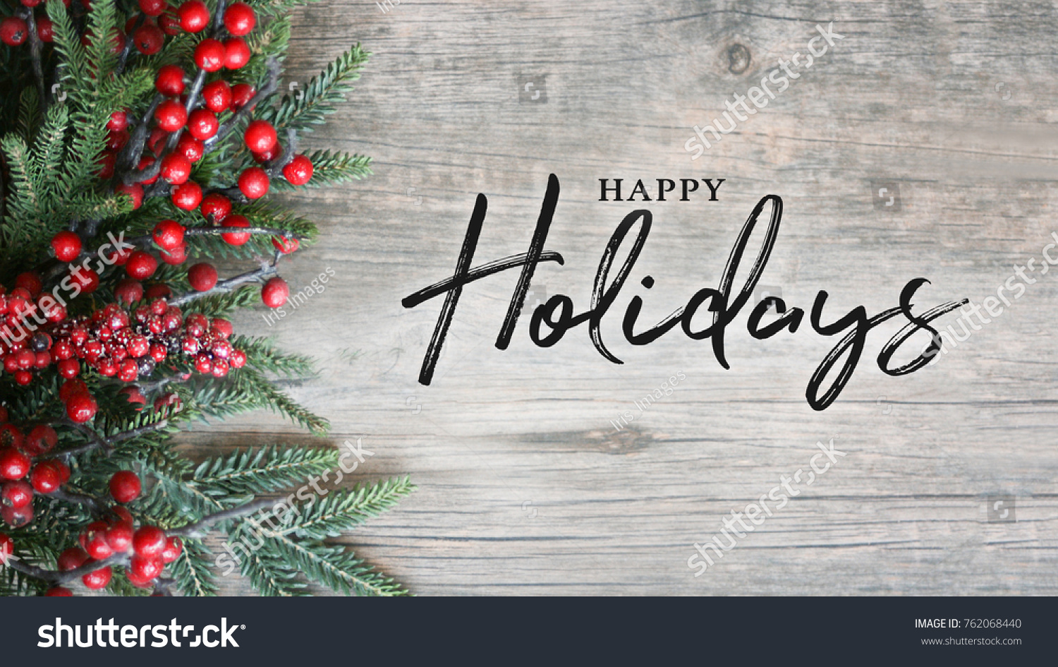 Happy Holidays Text with Holiday Evergreen Branches and Berries in Corner Over Rustic Wooden Background #762068440