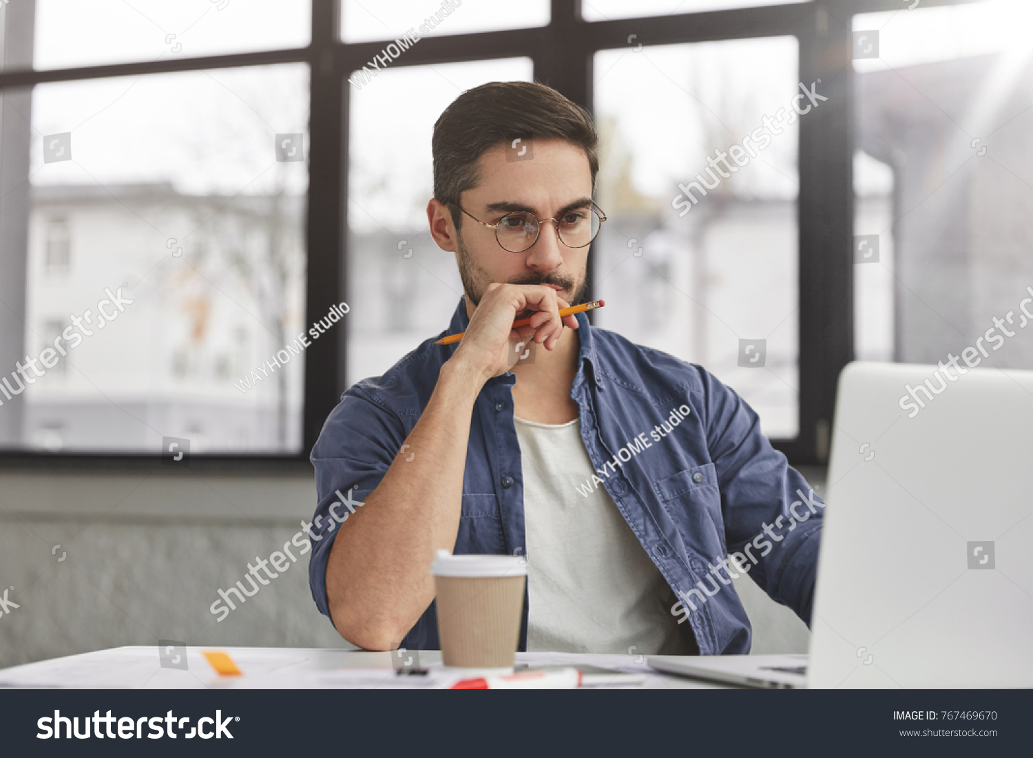 View of concentrated talented skilled male focused on screen of laptop computer, reads necessary information for creating budget report, drinks hot beverage. Attractive male freelancer keyboards text #767469670