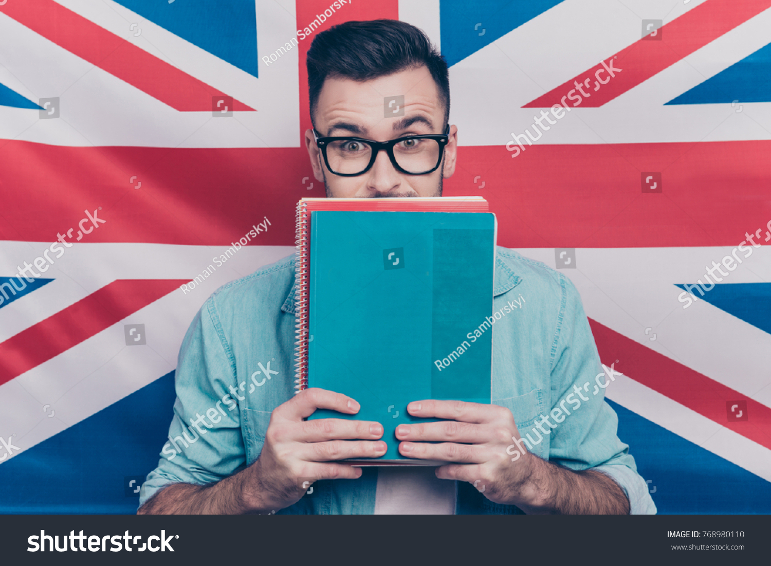 English language learning concept-portrait of excited man holding colorful copy books in hands closing half face with notebooks standing over English flag background #768980110