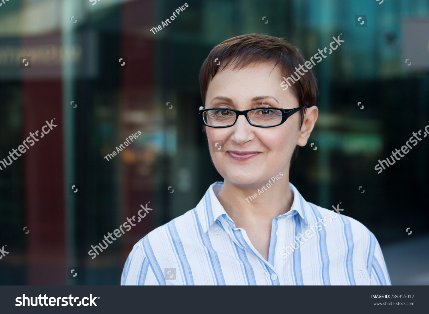 Older business woman headshot. Close-up portrait of executive, teacher, principal, CEO. Confident and successful middle aged woman 40 50 years old wearing glasses and shirt and smiling #789955012