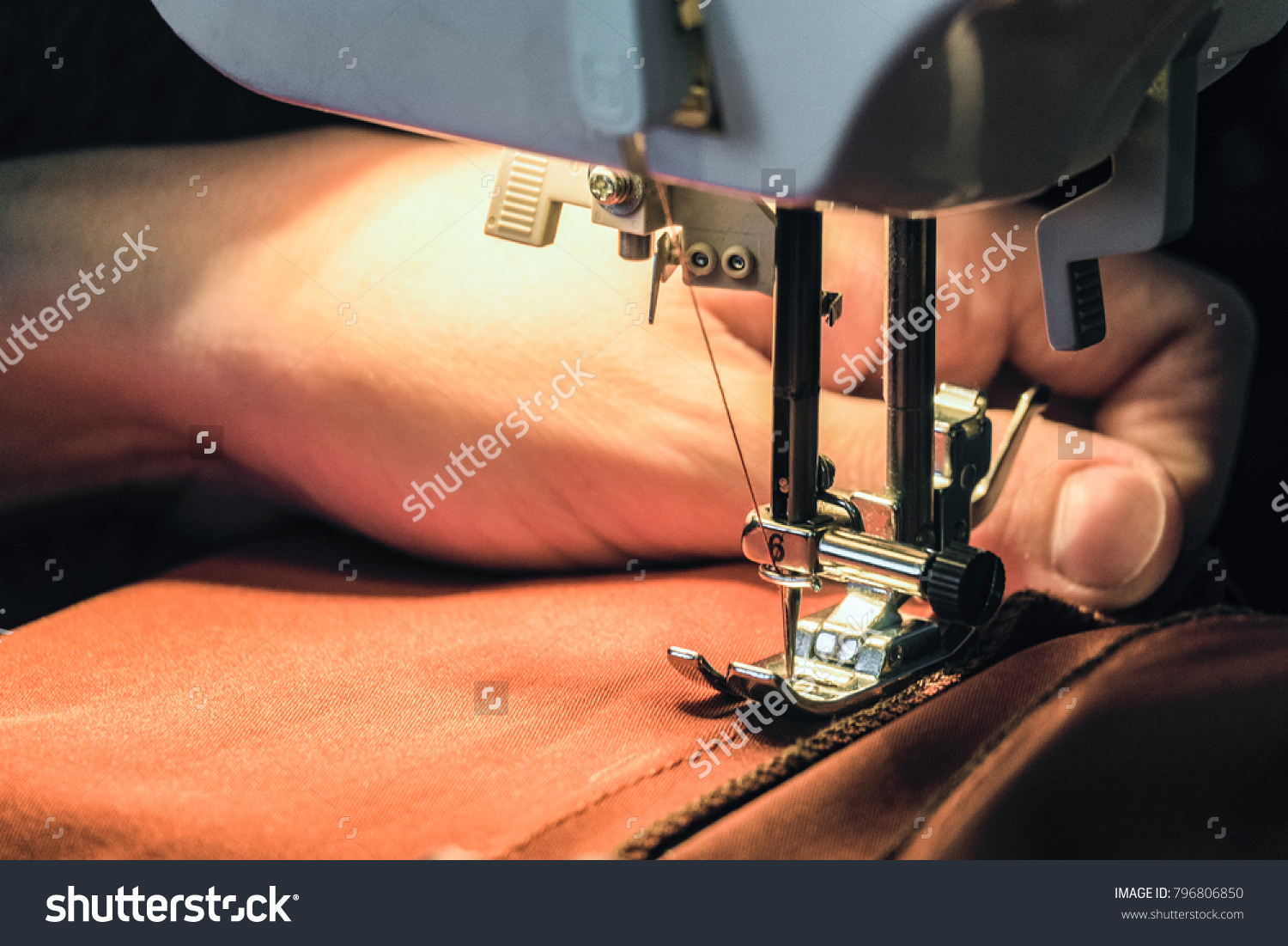Seamstress sews clothes made of red cloth on a sewing machine. Work by the light of the built-in hardware lamp. Steel needle with looper and presser foot close-up. #796806850