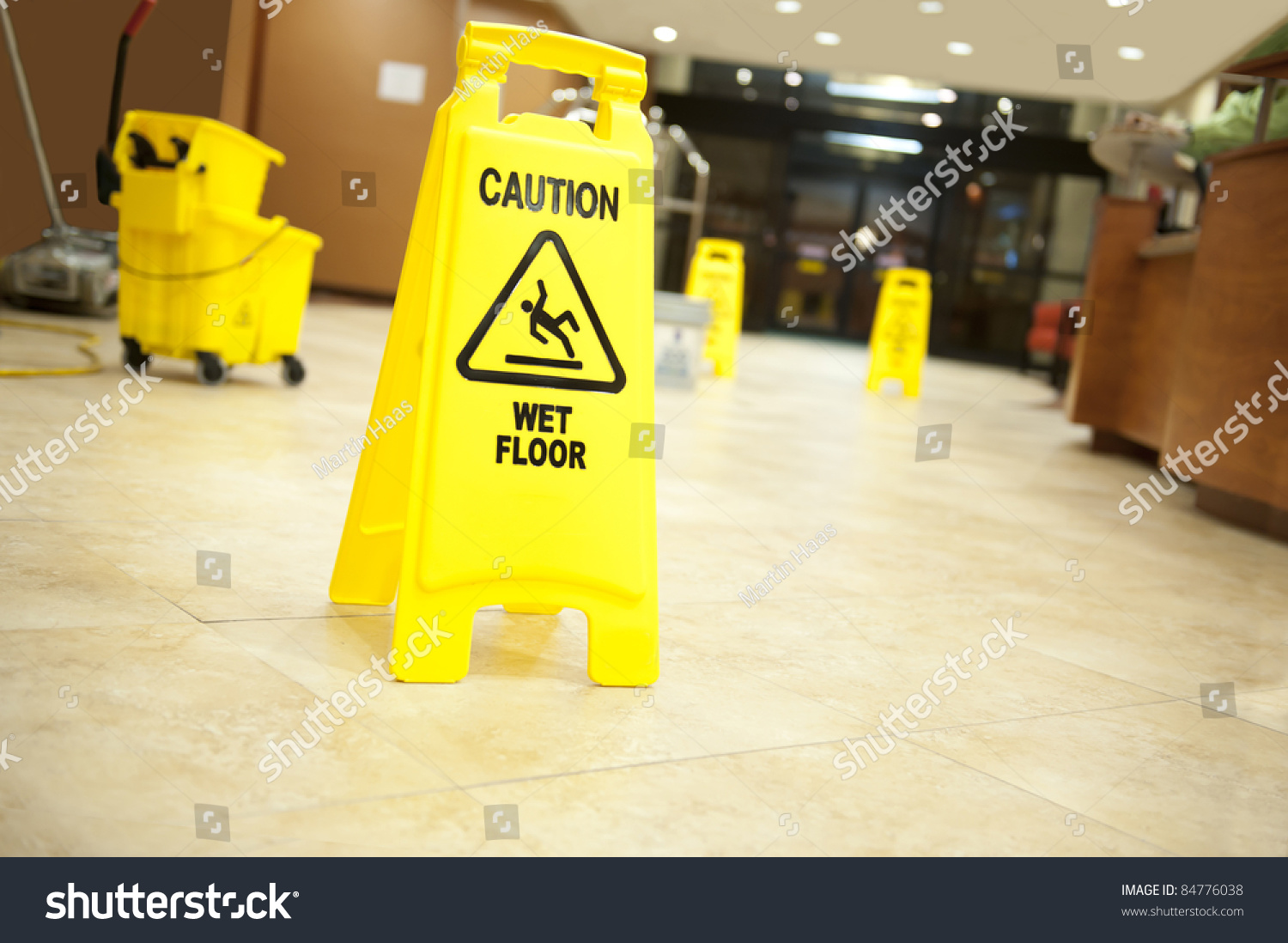 Lobby floor with mop bucket and "caution wet floor" signs, selective focus on nearest sign #84776038