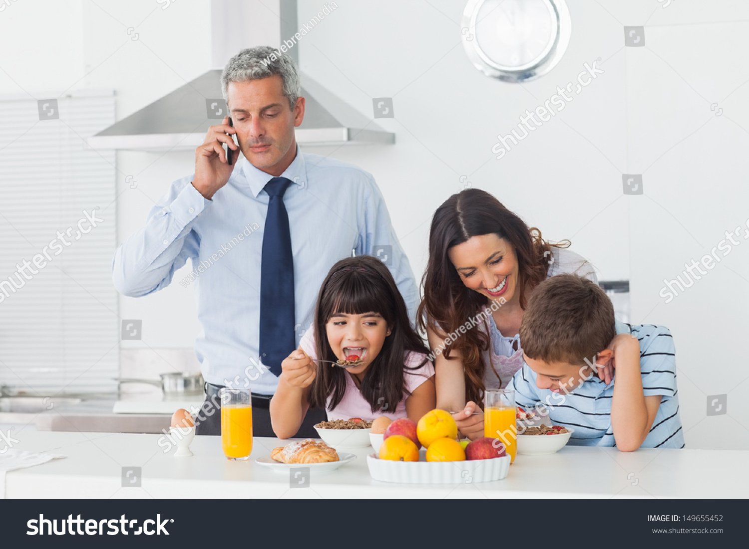 父亲打电话用手机与家人在家吃早餐在厨房里-