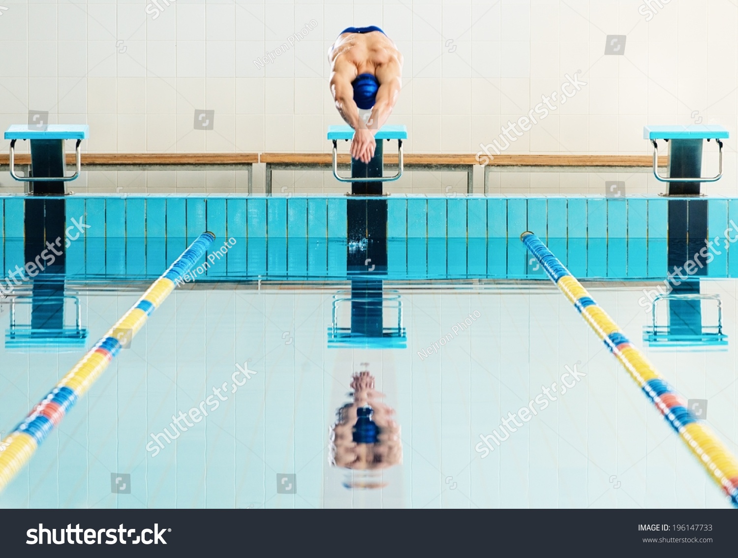 年轻肌肉游泳运动员跳起跑架在一个游泳池-人