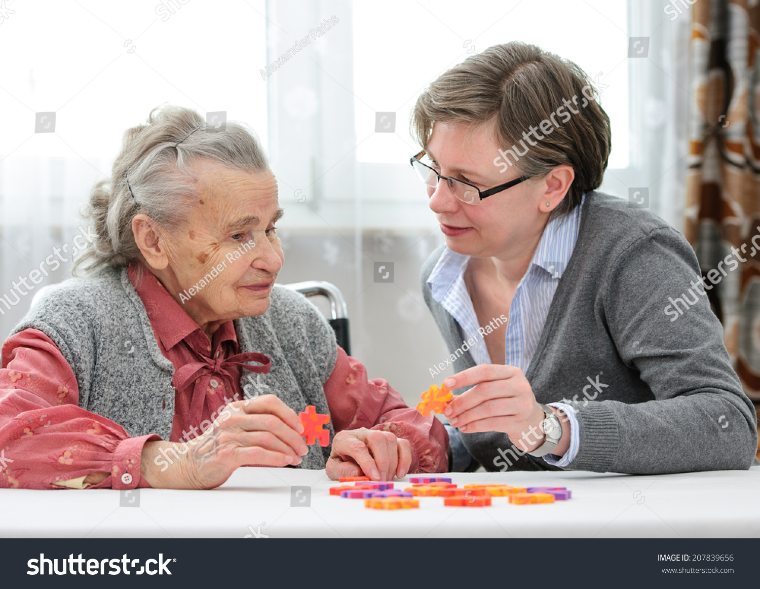护士照顾老人疗养院和高级玩拼图游戏的女人-