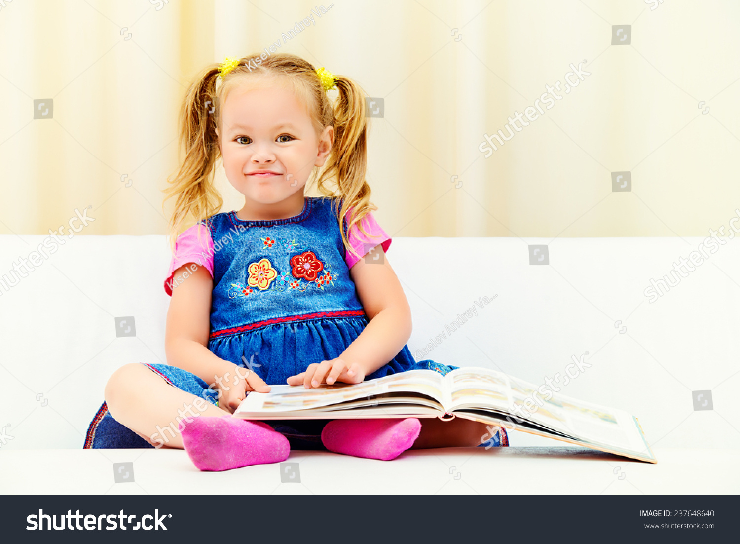 漂亮的小女孩坐在沙发上,看着一个儿童图画书