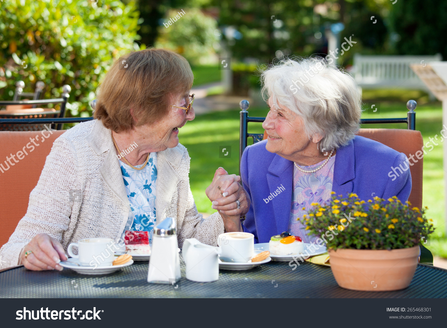 两个快乐的老年妇女在花园里聊天表与咖啡和点