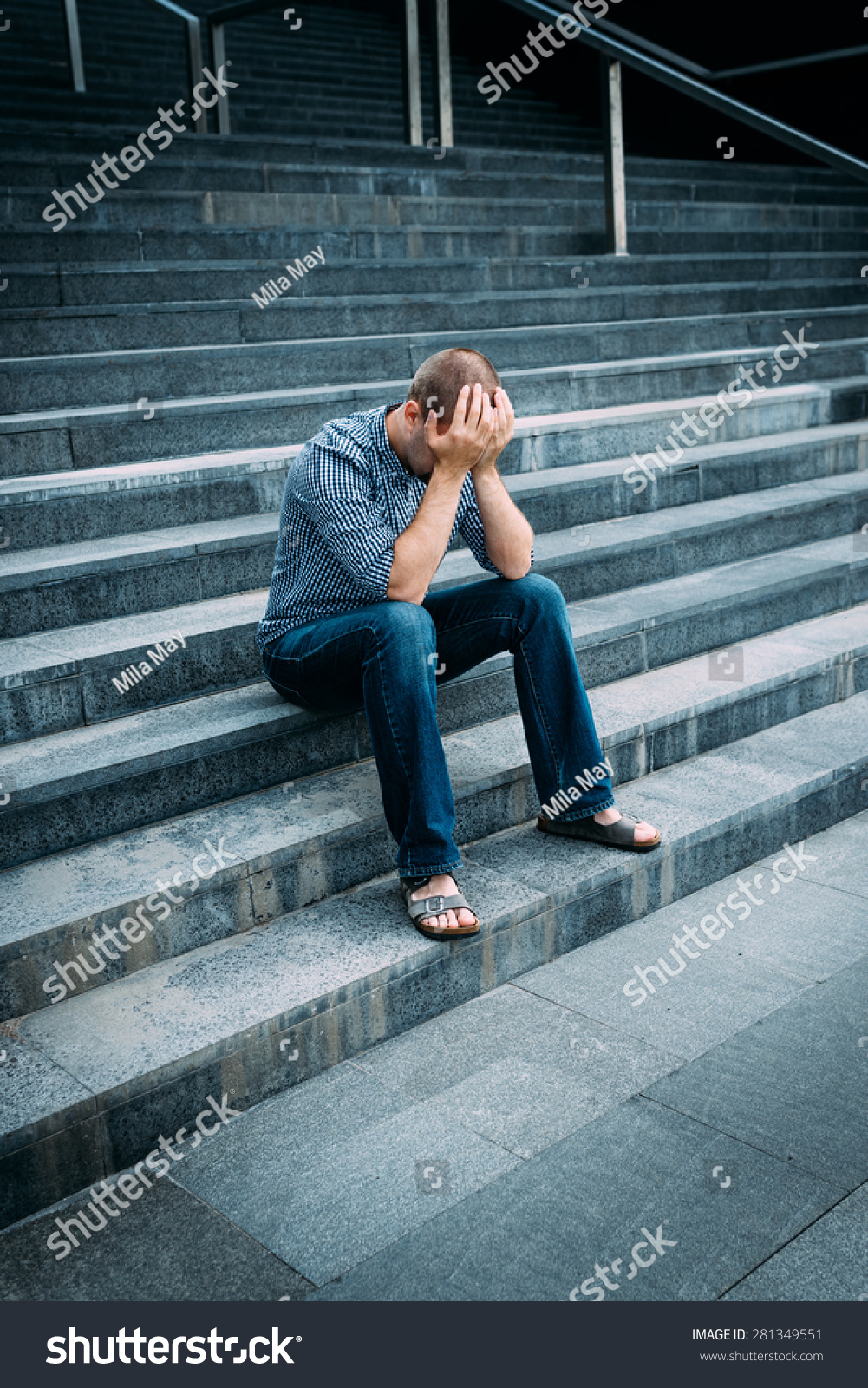 绝望的年轻人用双手捂着脸坐在楼梯的大建筑。