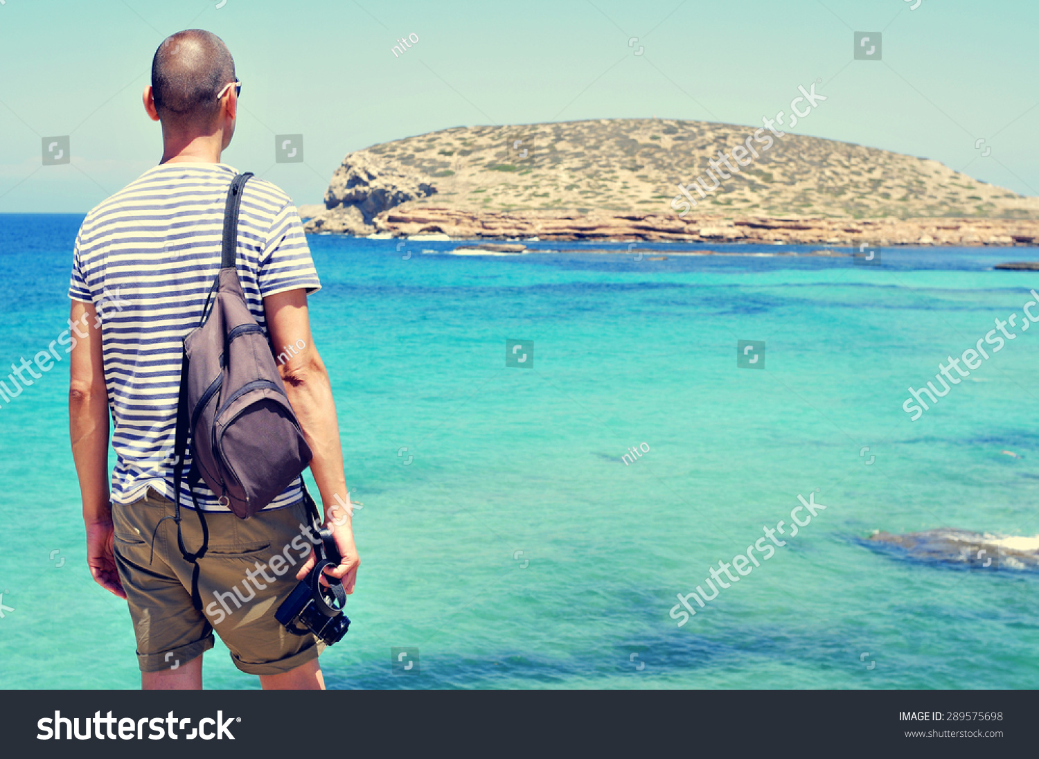 一个年轻人手里拿着相机看大海和Illa des博斯克