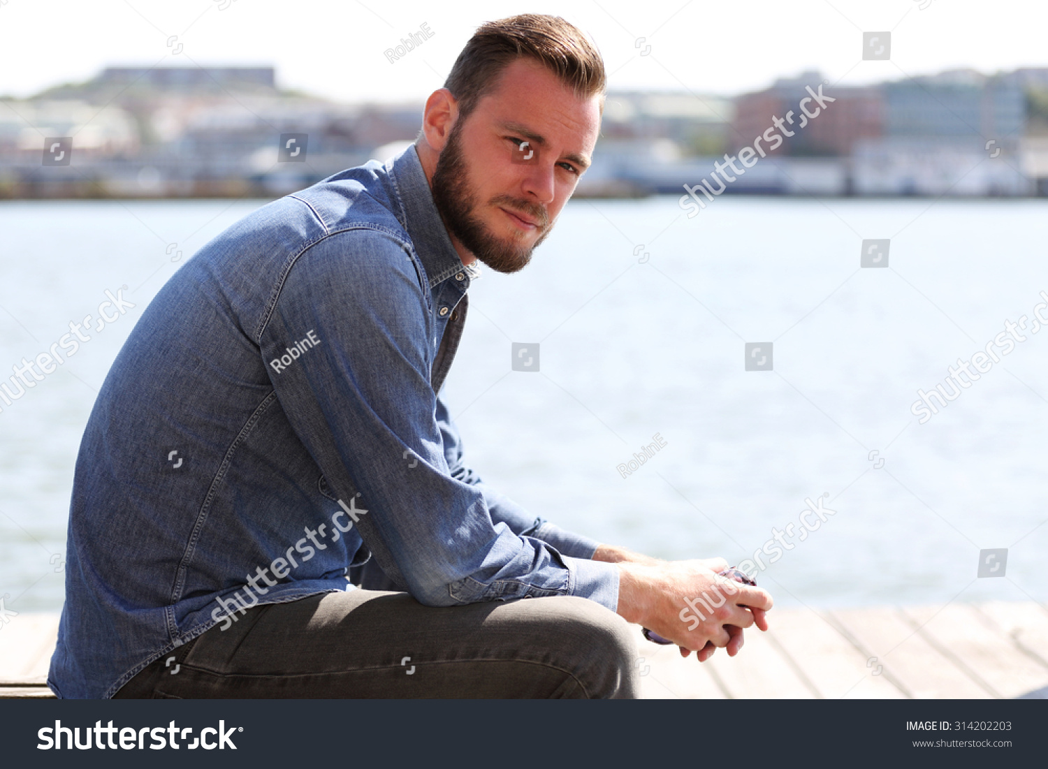 A Handsome Man Sitting Down Outside Wearing A Jeans Shirt With The ...