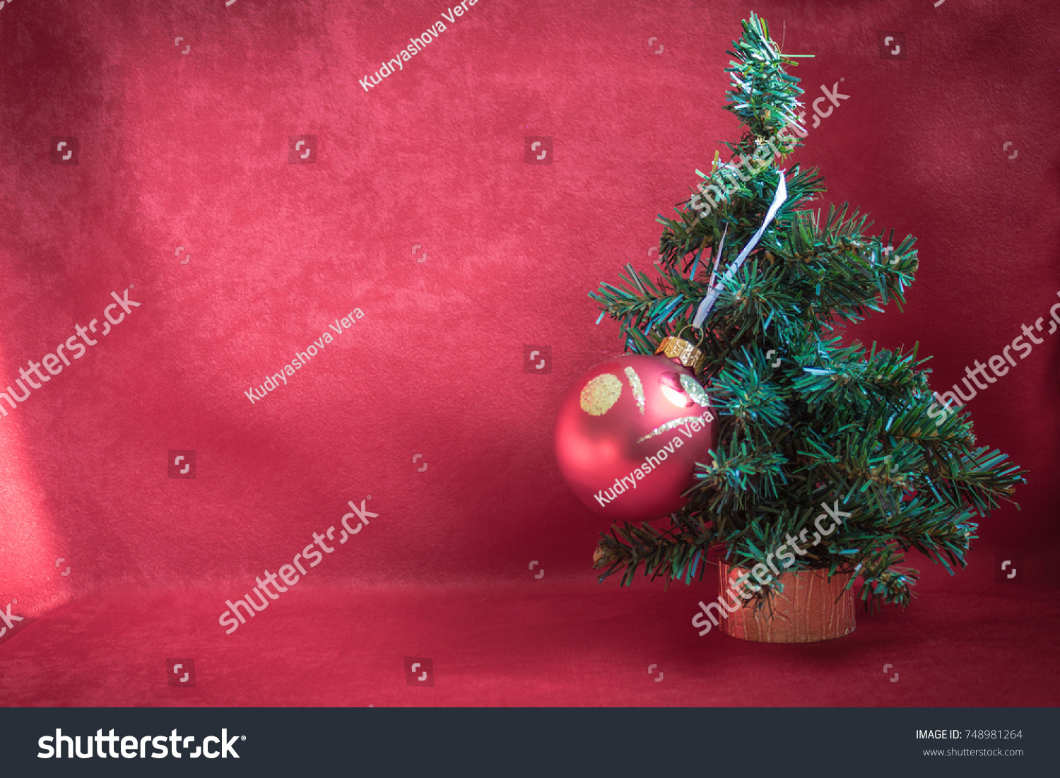 A Small Christmas Tree On Gold Stand Is Decorated With One Big Red Ball A Small Christmas Tree On Gold Stand Is Decorated With One Big Red Ball