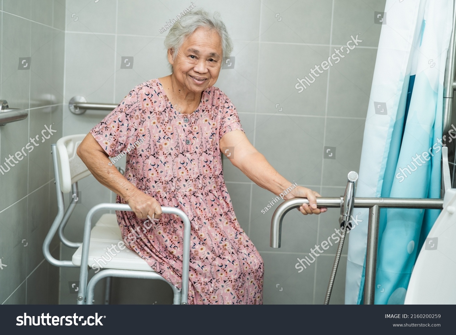 An elderly woman is sitting on a chair in a bathroom.