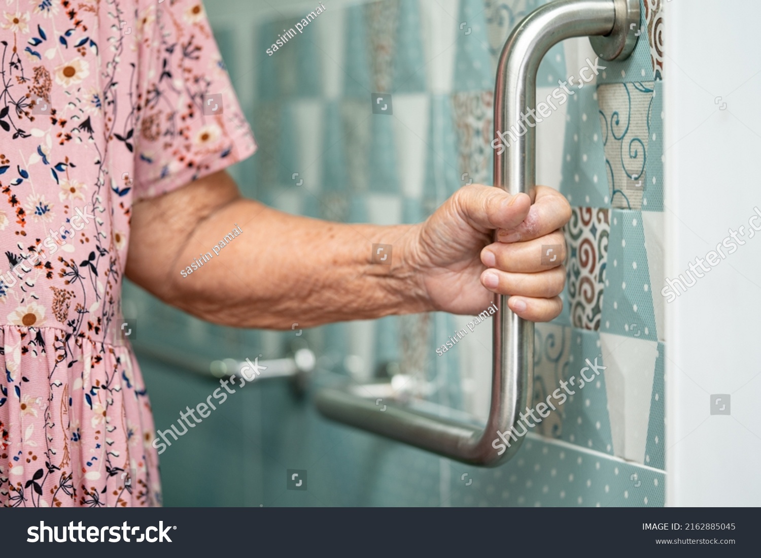 An elderly woman is holding a stainless steel handle in a bathroom.