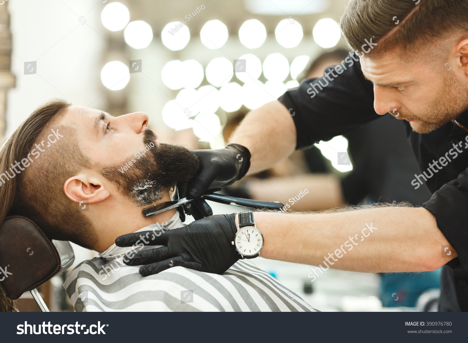 Stock Photo Attractive Barber Wearing Black Shirt Gloves And Watch Making A Beard Form With Razor For Man With 390976780 