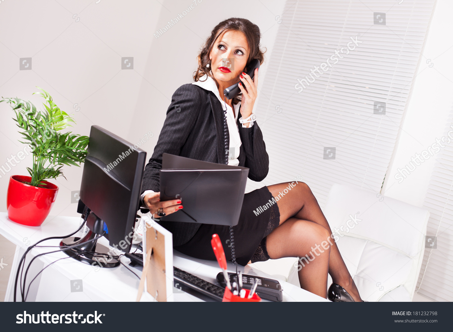 Attractive Coquettish Secretary Sitting On Desk Stock