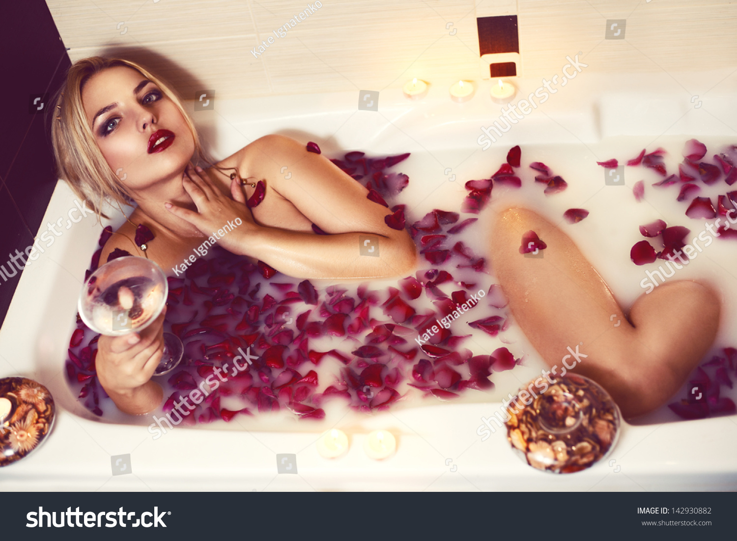 Stock photo sexy beautiful naked brunette woman laying in a bath with milk and red romantic falling rose