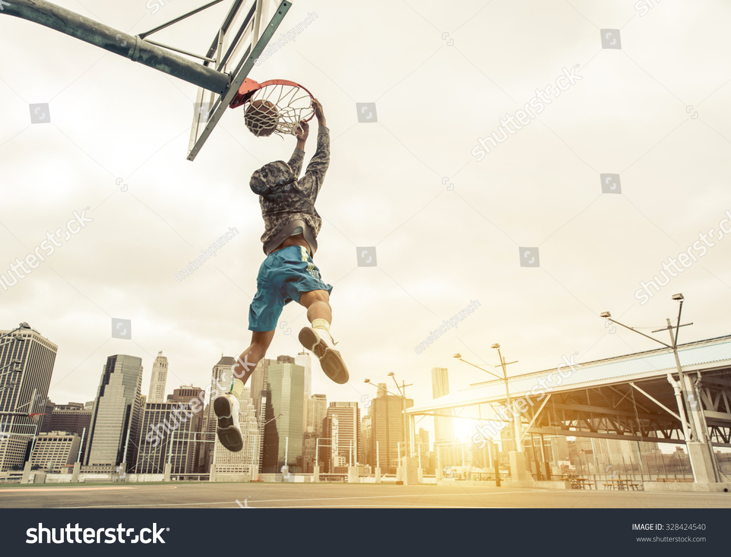 バスケットボールのストリート選手がリヤスラムダンクを作る 背景にニューヨークとマンハッタンの建物 の写真素材 今すぐ編集