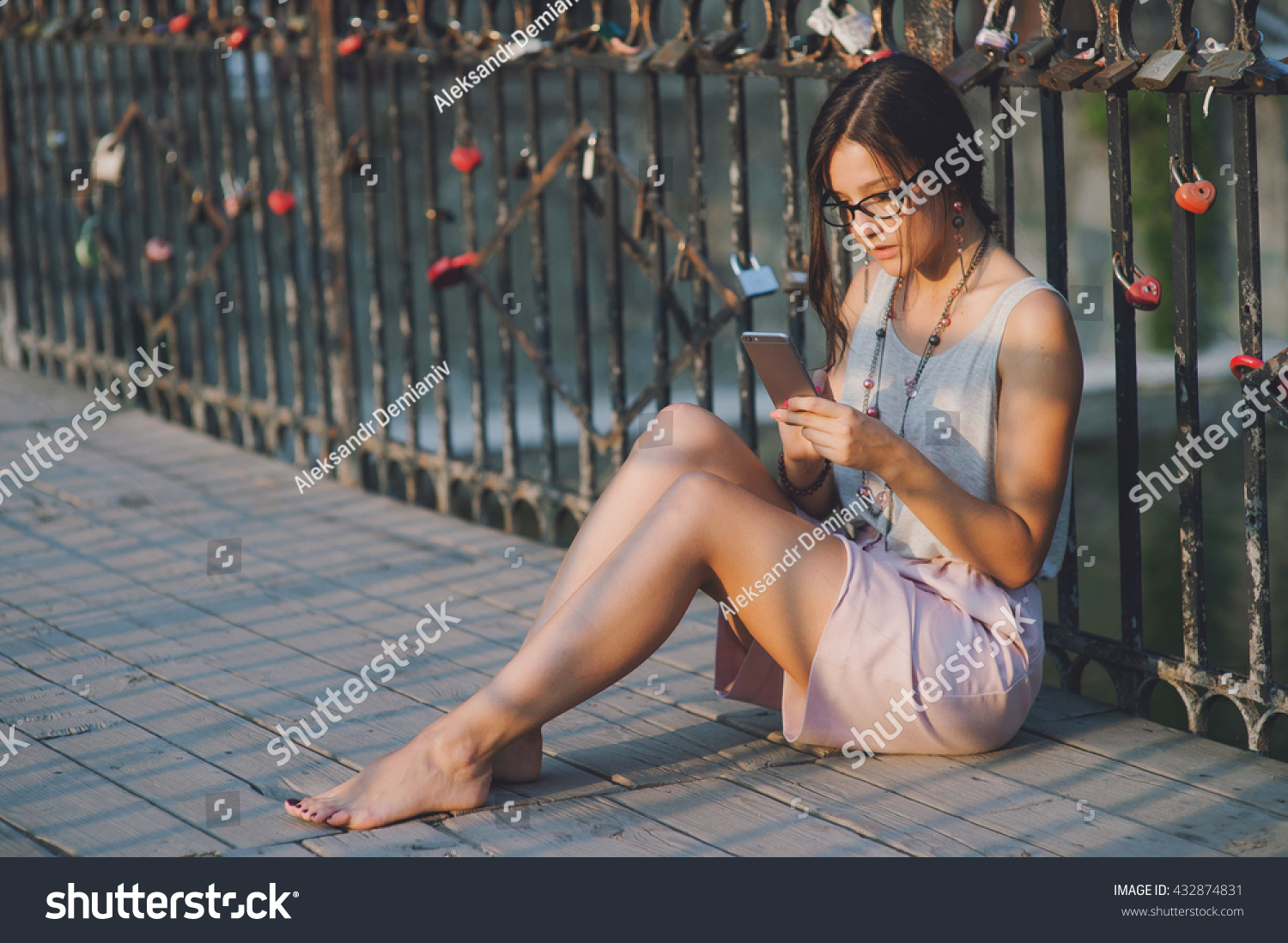 https://image.shutterstock.com/z/stock-photo-beautiful-girl-send-a-massage-with-a-smart-phone-sitting-on-a-bridge-evening-sunset-432874831.jpg