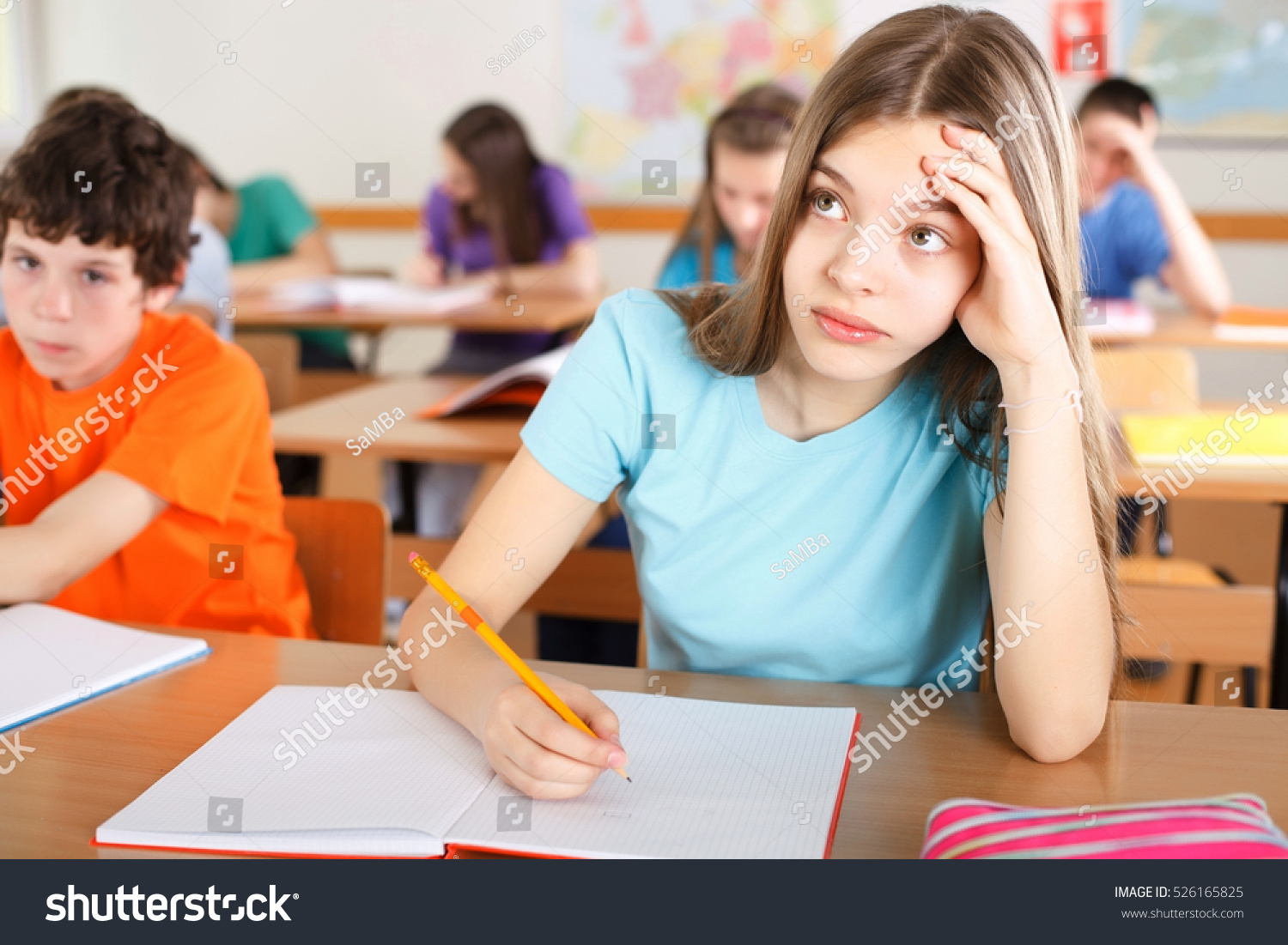 Beautiful Pensive Girl At Class Doing Schoolwork Other Students In Class Behind Her