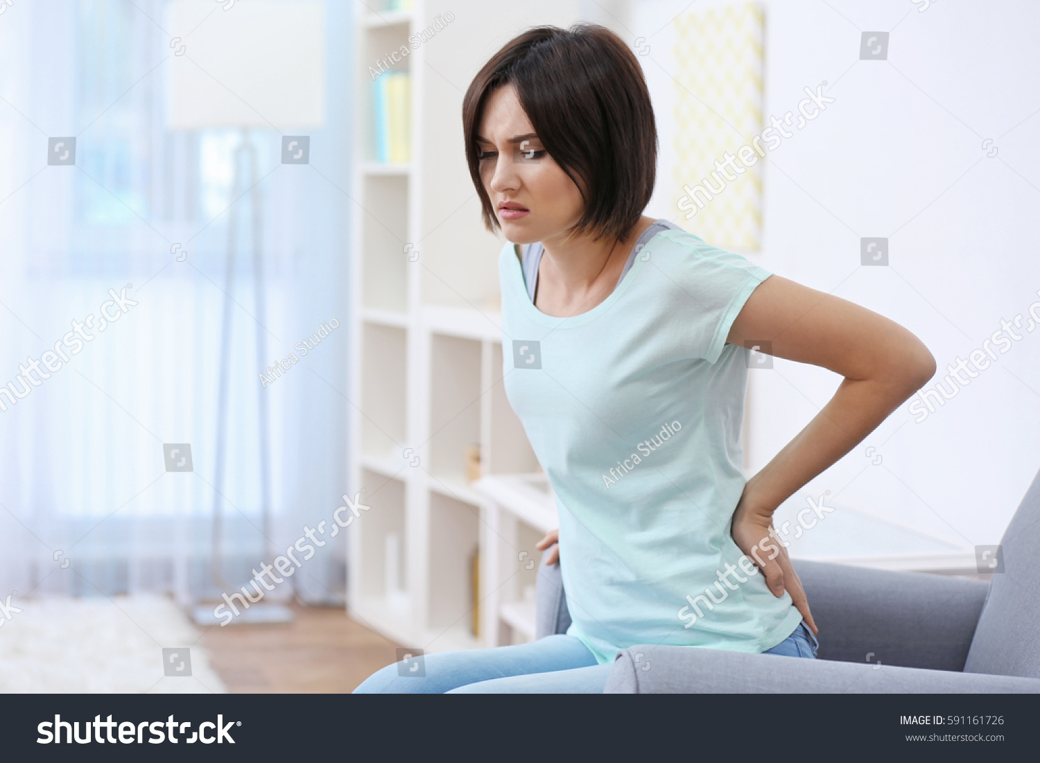 Beautiful young woman suffering from backache at home