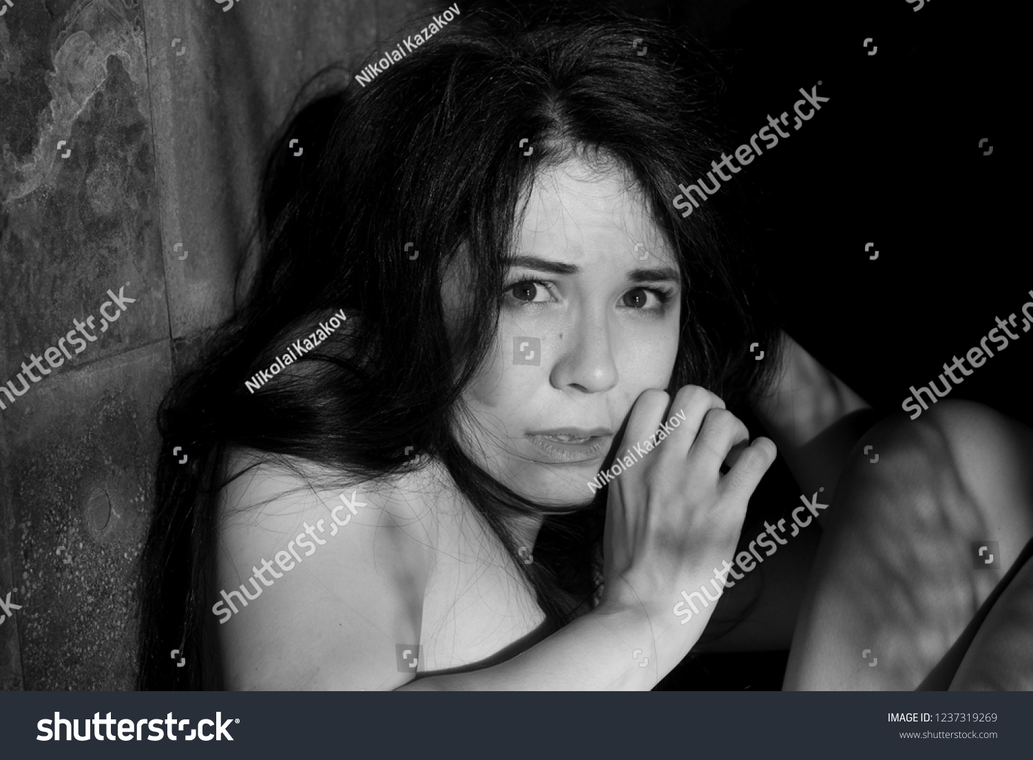 Black and white emotional portrait of a frightened and tense young woman looking out the window