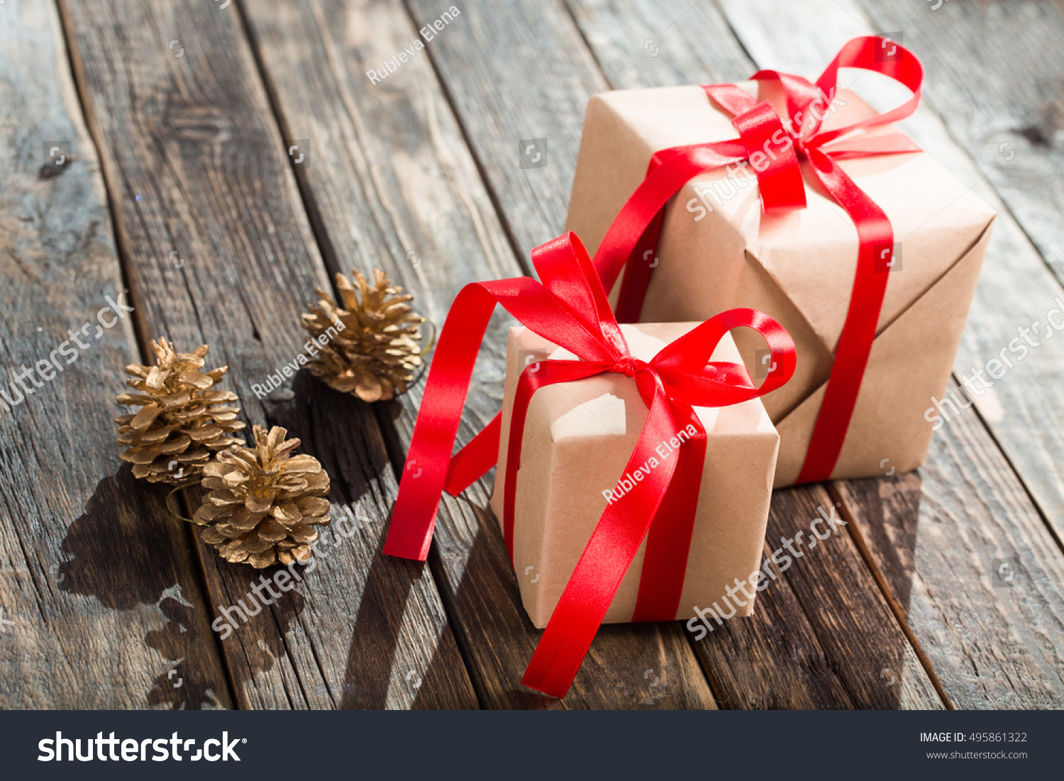 Christmas Gifts Packaged In Kraft Paper And Red Ribbon Constricted On Wooden Table With Space