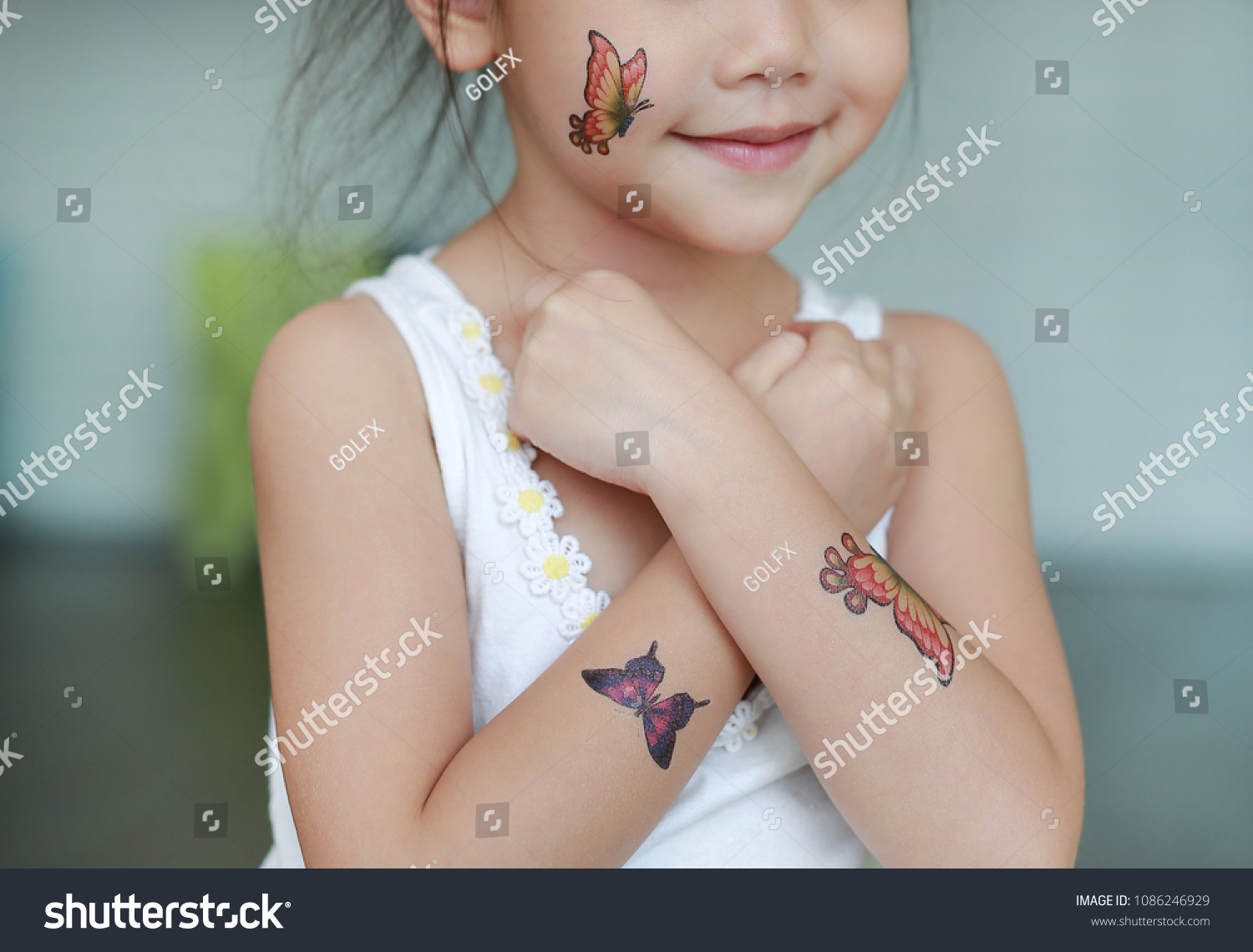 体の皮に蝶の刺青のステッカーを貼った小さな女の子の接写 タトゥーのドレスアップ の写真素材 今すぐ編集