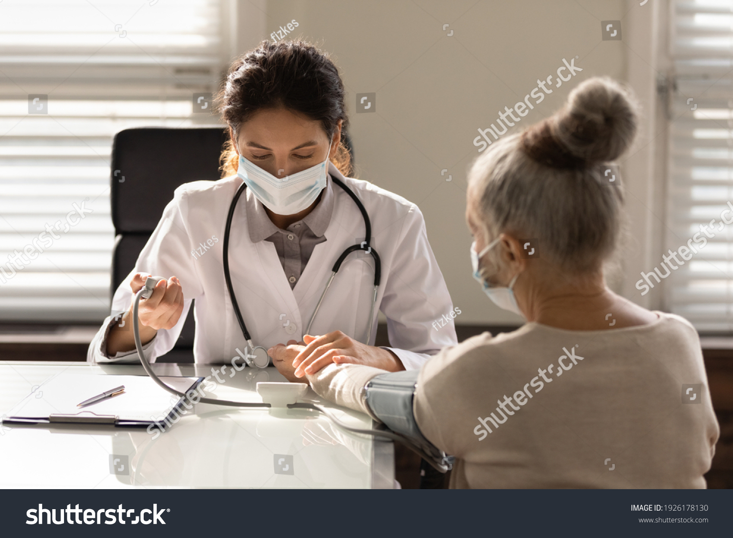 Close up serious female doctor wearing face mask measuring checking old woman blood pressure, using digital tonometer, medical checkup, elderly generation healthcare and insurance concept