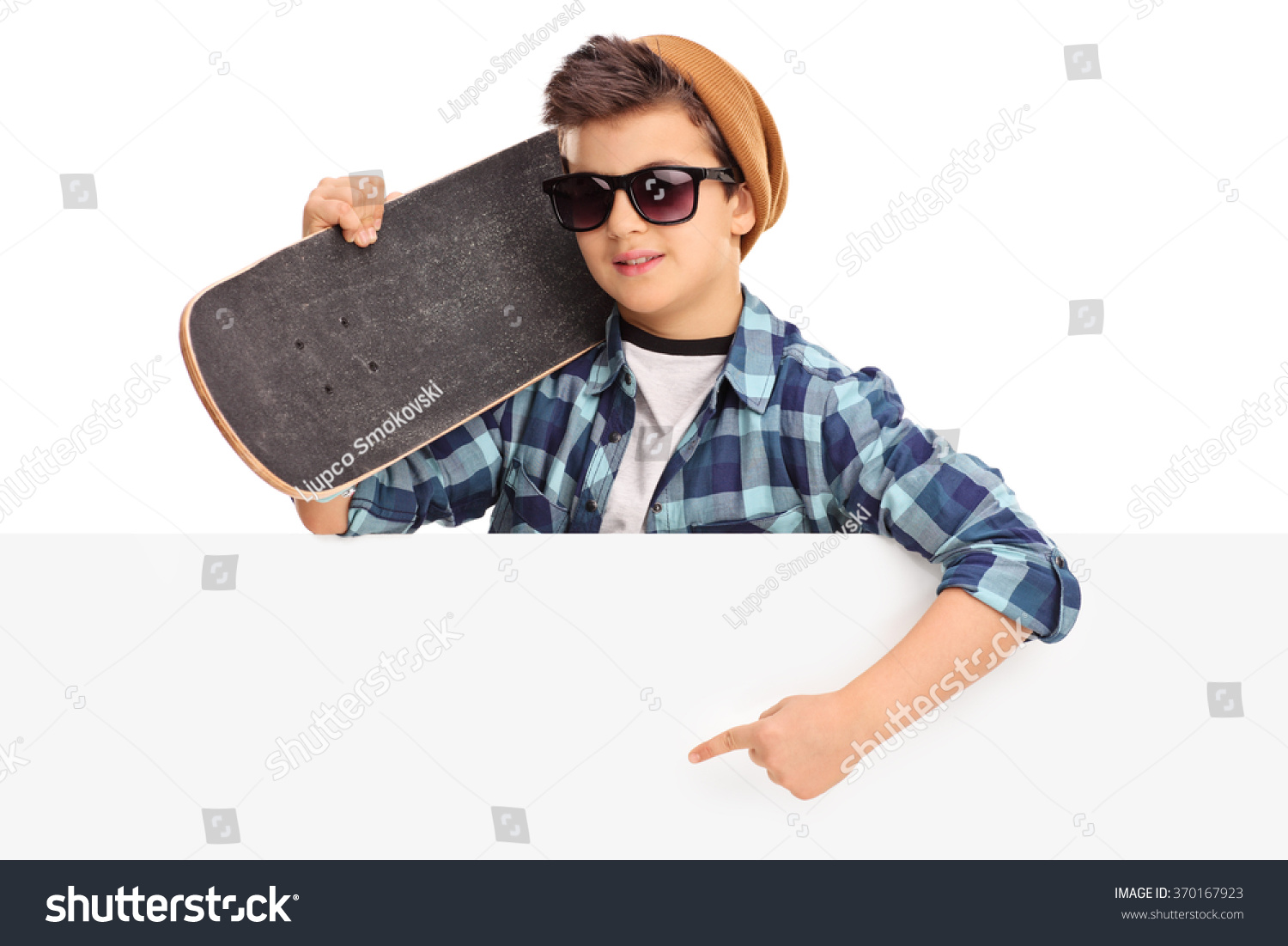 Cool Kid Holding A Skateboard And Pointing On A Blank Panel With His Hand Isolated On White Background