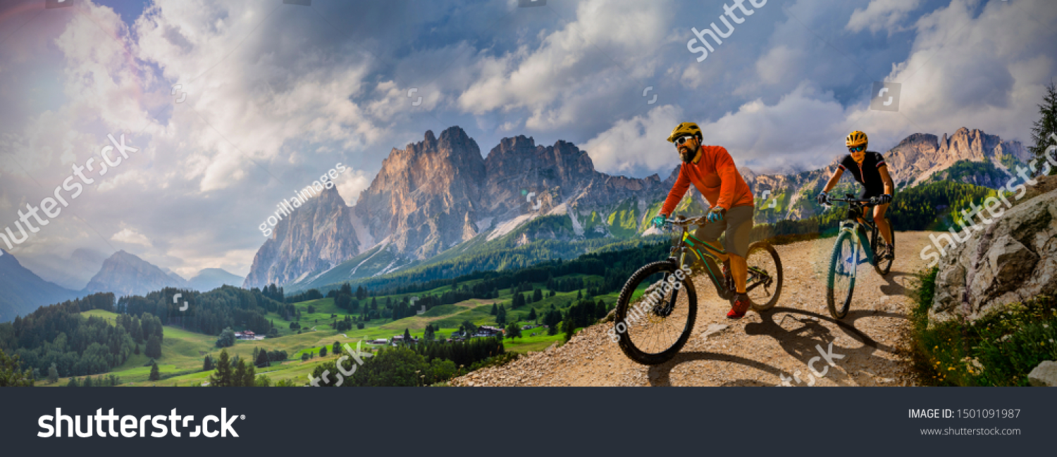 Couple cycling on electric bike, rides mountain trail. Woman and Man riding on bikes in Dolomites mountains landscape. Cycling e-mtb enduro trail track. Outdoor sport activity.