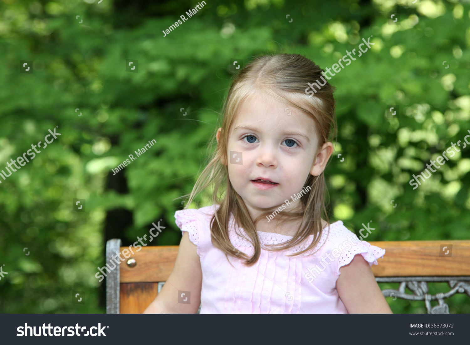 Cute 2 Year Old Girl Sits On A Park Bench With Very Expressive Eyes ...