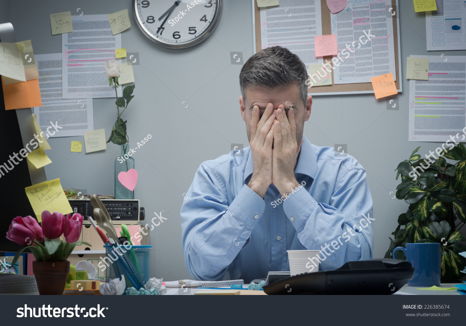 Exhausted Office Worker With Head In Hands Sitting At His Office Desk ...