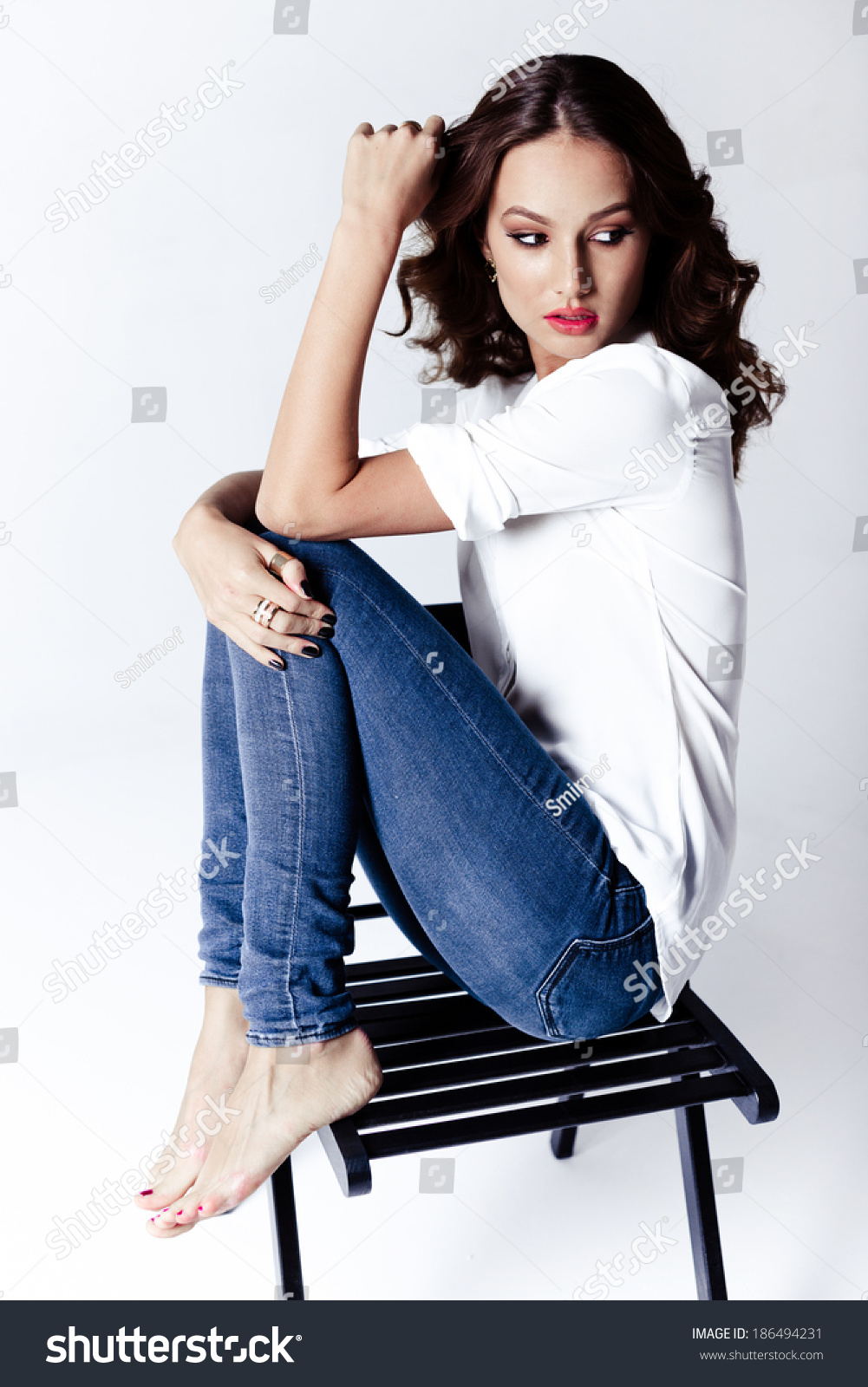 Fashion Model Sitting On A Chair In A Blouse And Jeans Barefoot On A ...