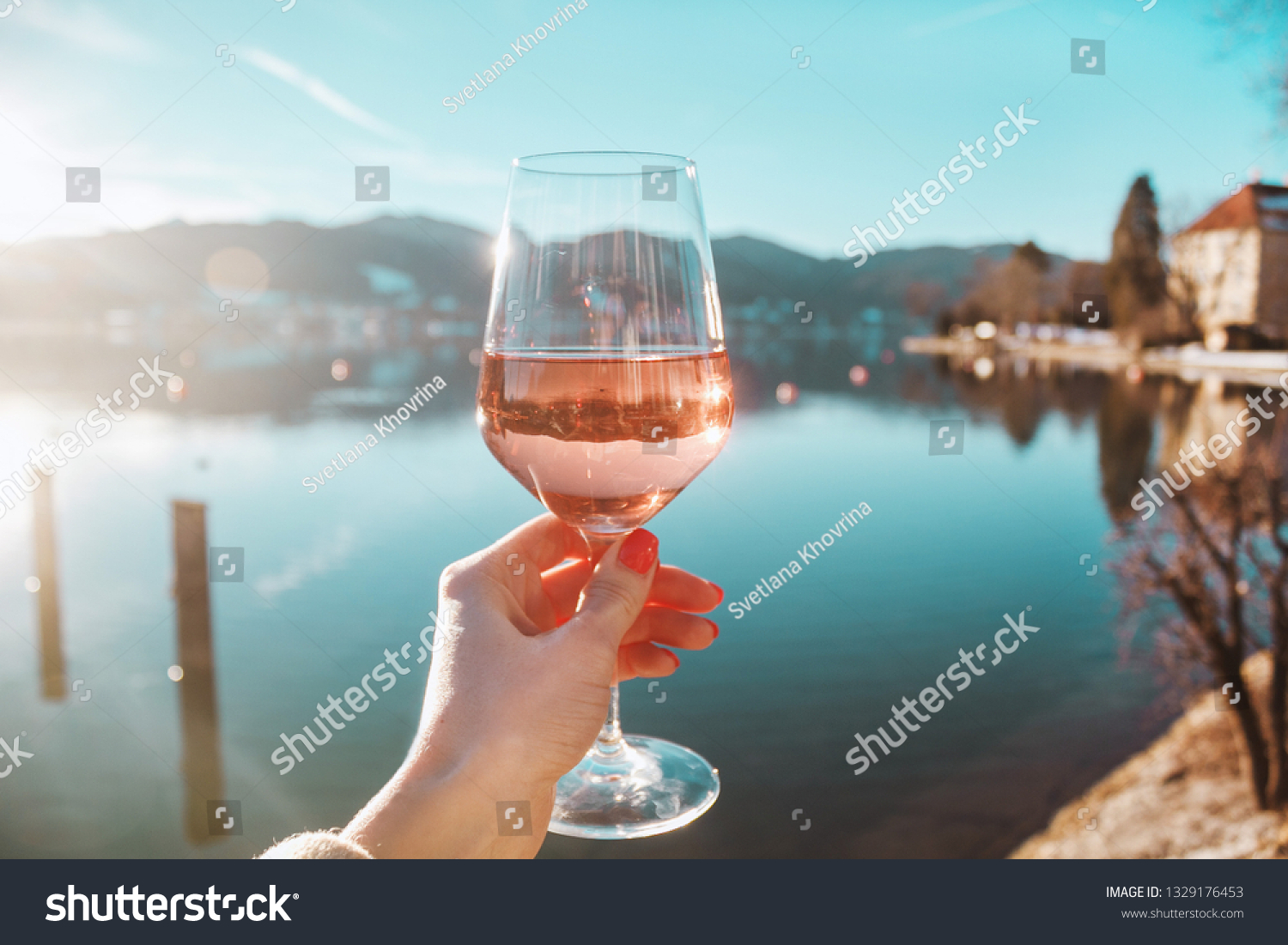 Female hand with glass of wine. Cozy pier on the coast of the lake Tegernsee. Alpine mountains in Bavaria (Bayern). Mountain view, beautiful landscape in Germany. Adventure in Europe (travel photo). 